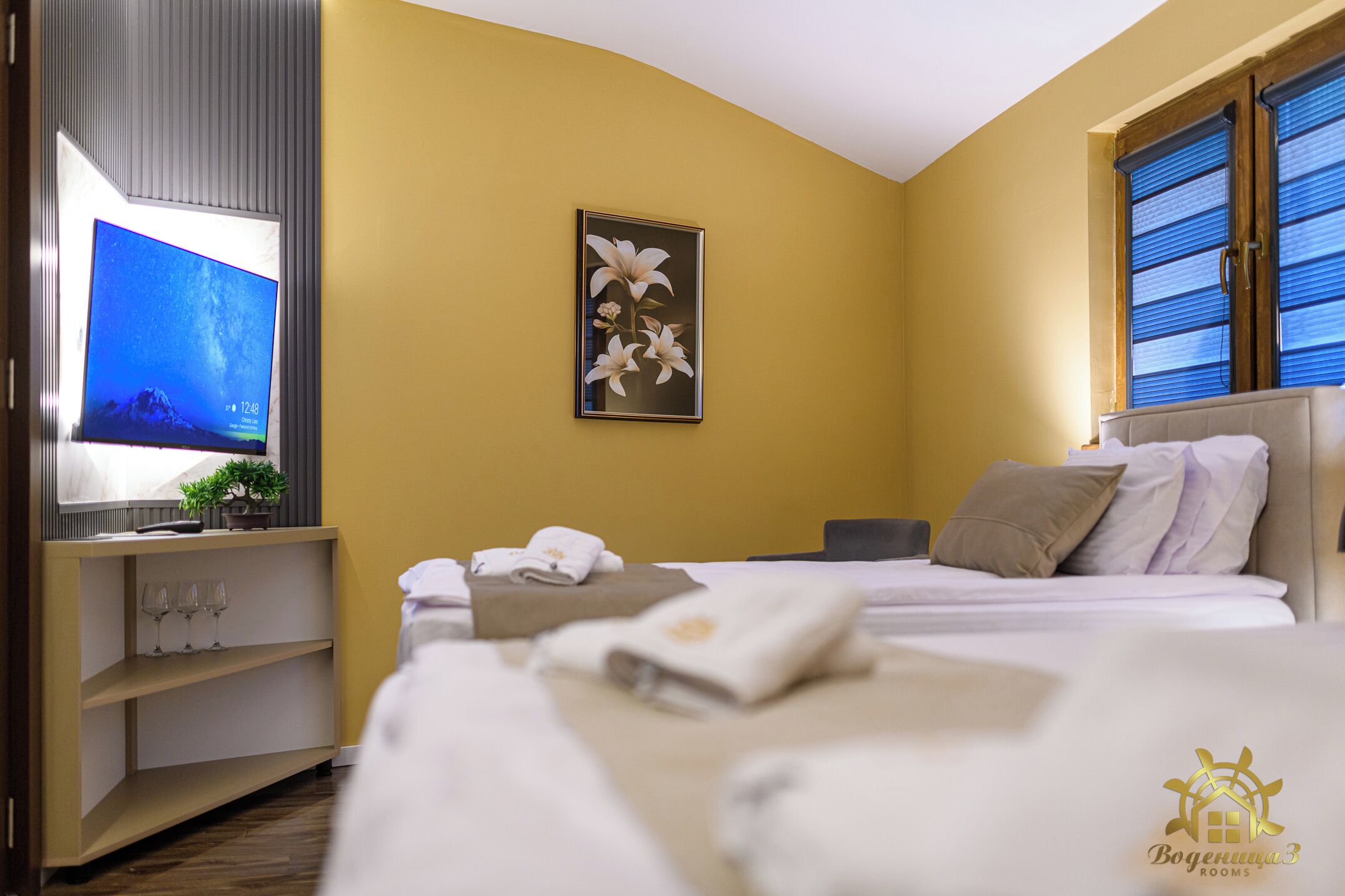 Une chambre d’hôtel avec un lit, une télévision, un tableau et une fenêtre avec des stores.