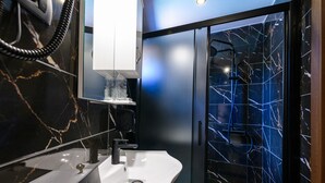 Une salle de bain moderne avec un pare-baignoire en marbre, un lavabo blanc et une douche à parois de verre.
