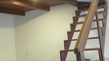 Una escalera de madera con barandilla de metal que conduce a una zona superior. Un sofá estampado se ve en primer plano.