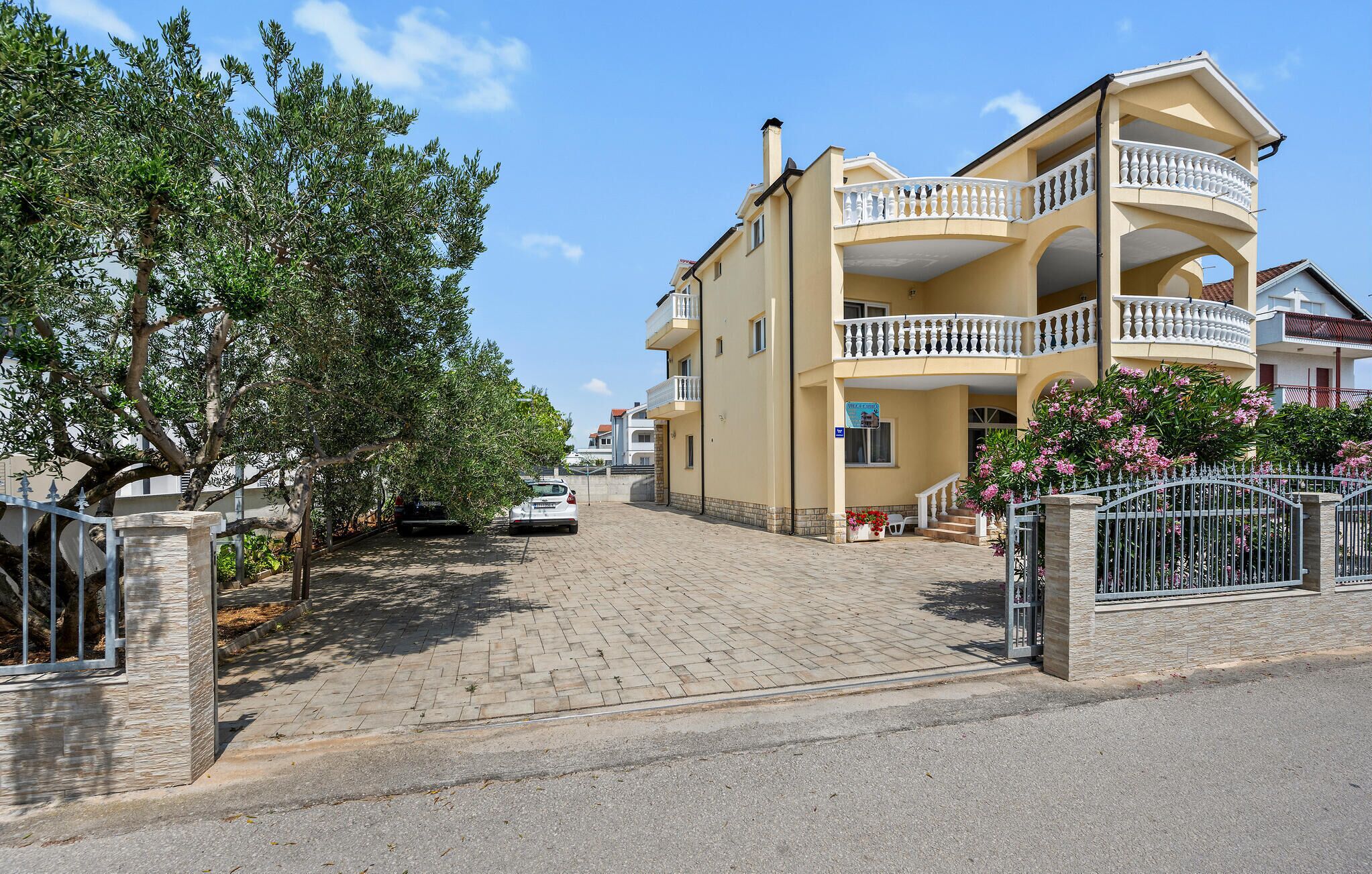 Een woonhuis met twee verdiepingen, een balkon, een verharde oprit en een boom.