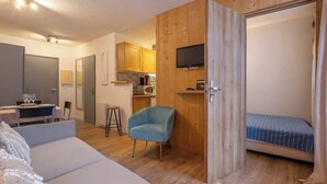 Un espacio habitable compacto con sofá, una pequeña mesa de comedor con sillas, kitchenette, televisor montado en la pared y cama.