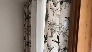 Una habitación con una cama, una puerta de madera y cortinas con un estampado de hojas tropicales.