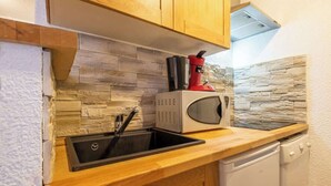 Cocina compacta con protector antibarrotes de piedra, un lavamanos, microondas y una cafetera roja.