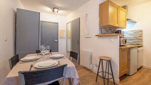 Un comedor compacto con una mesa dispuesta para cuatro personas, una pequeña cocina con lavavajillas y un radiador en la pared.