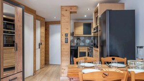A modern kitchen with wooden cabinetry, a dining area with a wooden table and chairs, and a large black refrigerator.