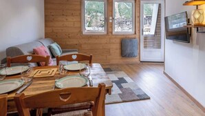 A dining area with a wooden table set for four, a sofa with heart-shaped cushions, and a TV mounted on the wall.
