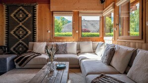 A cozy cabin interior with a wooden ceiling, a large window, and a sectional sofa.