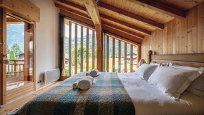 A wooden bedroom with a large bed, a view of the outdoors, and a wooden ceiling.
