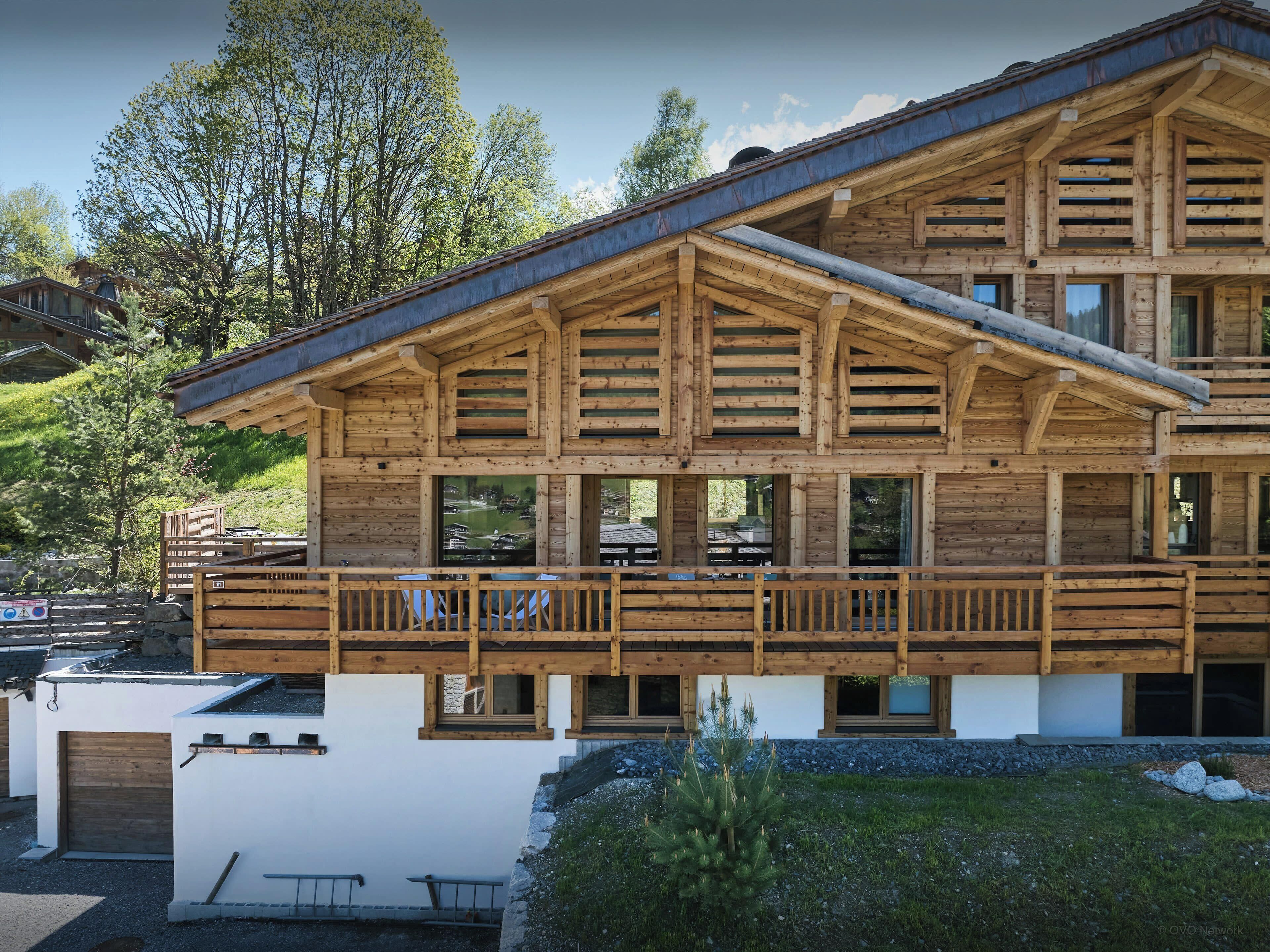 A wooden chalet with a balcony, large windows, and a white facade.
