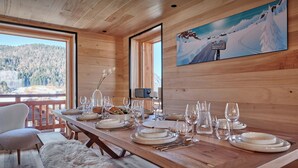 A wooden dining table set with plates, glasses, and cutlery, overlooking a snowy mountain landscape.