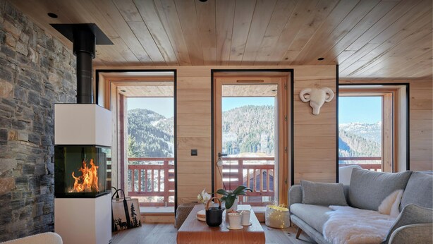 A cozy living room with a fireplace, wooden furniture, and large windows offering mountain views.