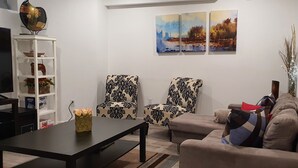 Ein Wohnzimmer mit einer Couch, zwei gemusterten Sessel, einem Couchtisch und einer weißen Regaleinrichtung mit Dekorationselementen.