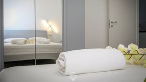 Una camera d'albergo con un letto, uno specchio, un asciugamano bianco e un comodino con una lampada.