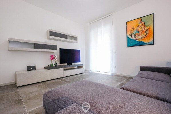 A modern living room with a flat-screen TV, a sofa, a painting, and a window with curtains. - Blue Bay Alghero Blue Bay Alghero (Alghero)