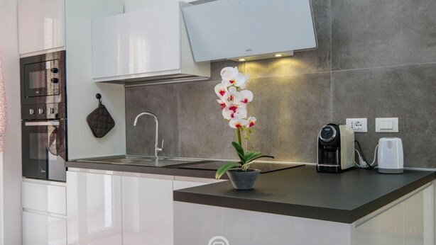 Una cucina moderna con forno integrato, macchina del caffè e un'orchidea in vaso sul bancone.