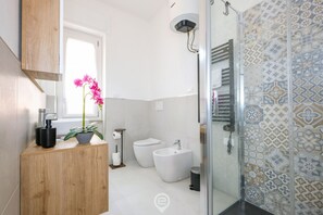 A modern bathroom with a wooden vanity, a toilet, a bidet, a shower, and patterned tiles. - Blue Bay Alghero Blue Bay Alghero (Alghero)