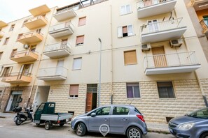 A multi-story residential building with balconies, a streetlight, parked vehicles, and a small truck. - Blue Bay Alghero Blue Bay Alghero (Alghero)