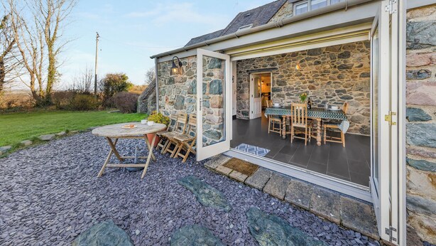 Une maison en pierre avec un patio, une table et des chaises, et une porte donnant sur l’intérieur.
