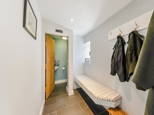 A hallway with a bench, a wooden door, a sink, and a coat rack with jackets.