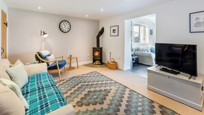 Un salon avec un canapé, un tapis à motifs, un téléviseur, une cheminée et une horloge au mur.