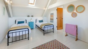 Une chambre avec deux lits, une fenêtre, une tapisserie murale et une porte en bois.