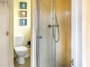A bathroom with a toilet, a shower with a glass door, and wall-mounted decorations. - 1 bedroom accommodation in St Mawes (St Mawes)