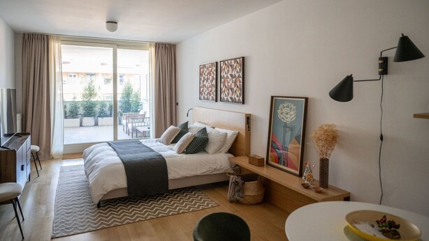 A modern bedroom with a large bed, a desk, and a view of the outdoors.
