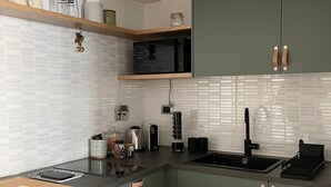 A modern kitchen with a black countertop, green cabinets, and a white tiled backsplash.