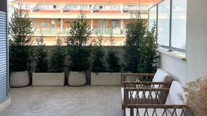 A balcony with potted plants, a wooden chair, and a view of a building in the background.