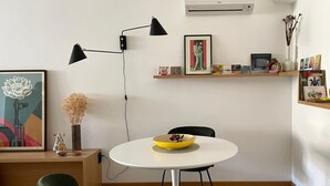 A modern living room with a round white table, two black floor lamps, a green chair, and a small shelf with decorative items.