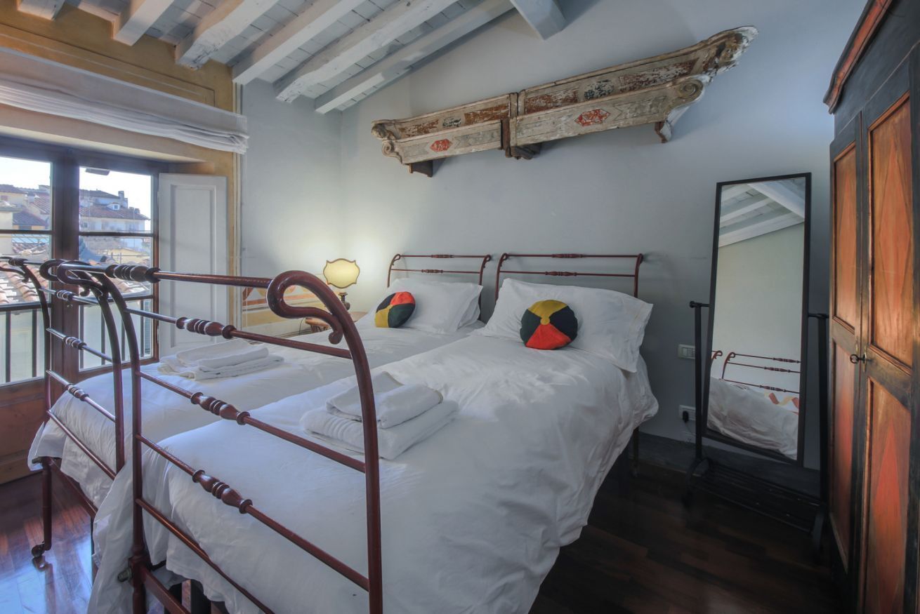 A room with a bed, a wooden ladder, a window, and a mirror.