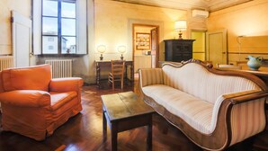 Une pièce avec un plancher en bois, un canapé, une chaise, une petite table, un meuble et une fenêtre donnant sur des immeubles.