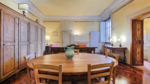 Une salle à manger avec une table ronde en bois, des chaises et un pichet. On aperçoit des armoires et un radiateur à l’arrière-plan.