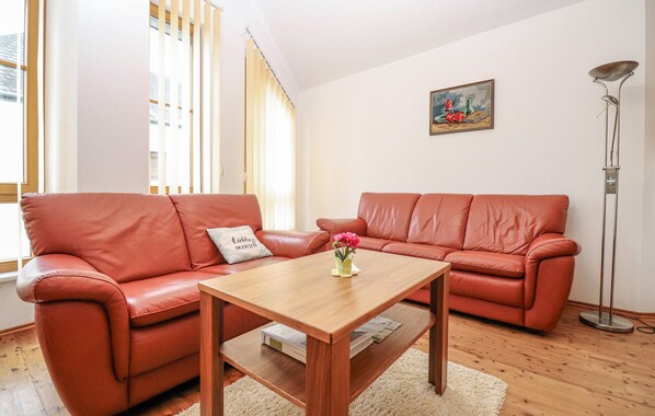 A living room with two red leather sofas, a wooden coffee table, a small vase with flowers, a framed picture on the wall, and a tall floor lamp. - Ferienwohnung in Stratzing (Stratzing bei Krems)