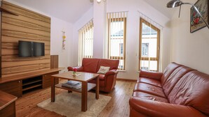 Ein Wohnzimmer mit einer Holzwand, einem Ledersofa, einem Couchtisch und einem an der Wand befestigten Fernseher.