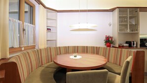Ein Essbereich in der Ecke mit einem runden Holztisch, einer gepolsterten Sitzbank mit Streifenmuster, einer Pendelleuchte und einem Schrank mit Glastüren, der Gläser beherbergt.