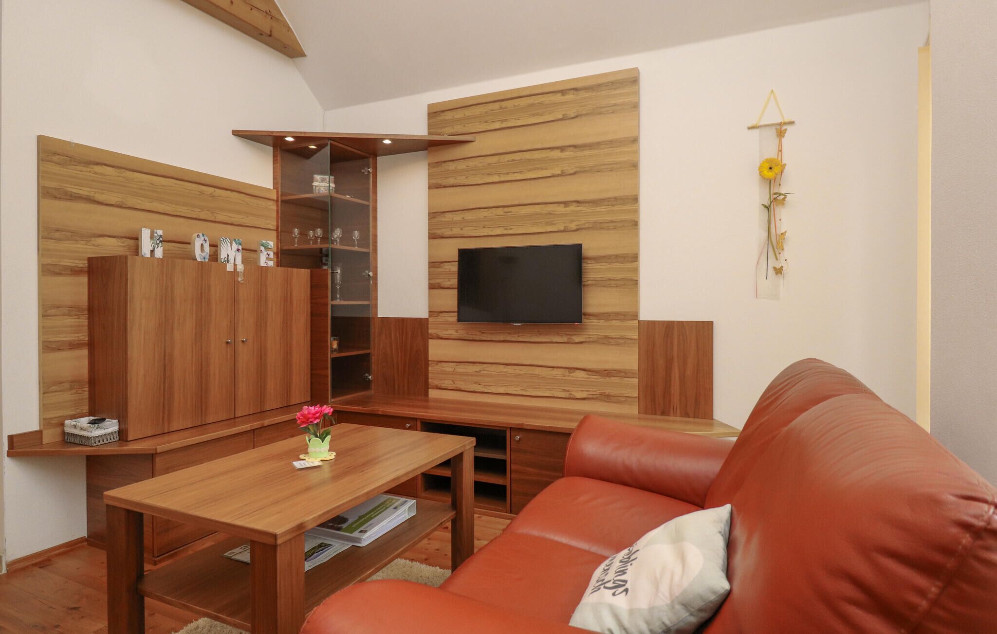 Een moderne woonkamer met een houten wandpaneel, een flatscreen televisie, een leren bank en een houten salontafel.