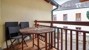 Ein Balkon mit Holztisch und -stühlen, einer kleinen Vase mit Blumen und Blick auf ein Gebäude mit roten Fensterrahmen.