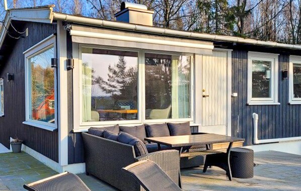 Un espace extérieur moderne aménagé avec une table et des chaises, de grandes fenêtres et une vue sur les arbres.