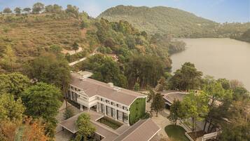 A modern hotel with a flat roof, surrounded by lush greenery and a lake.