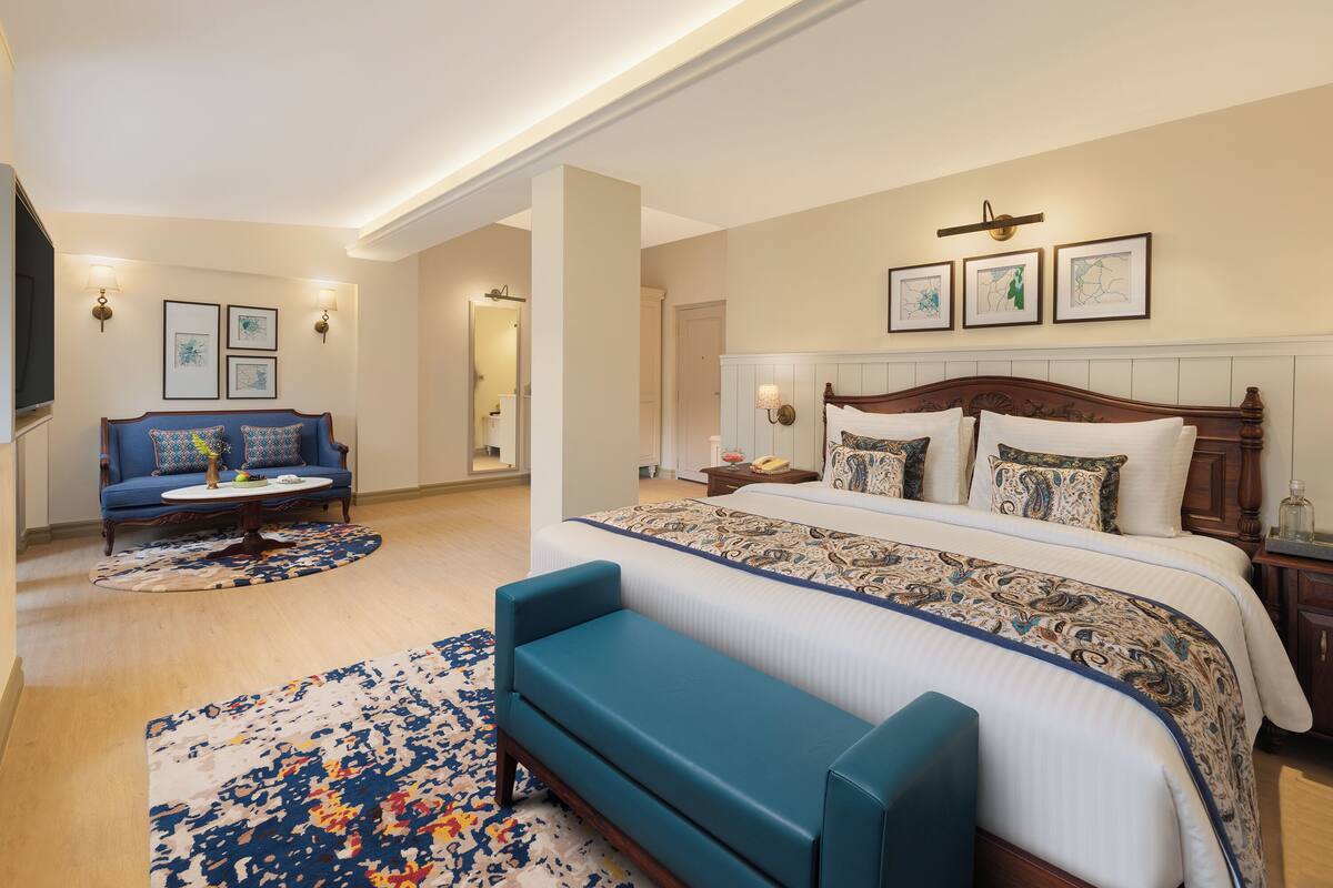 A hotel room with a large bed, a blue sofa, a patterned rug, and artwork on the walls.