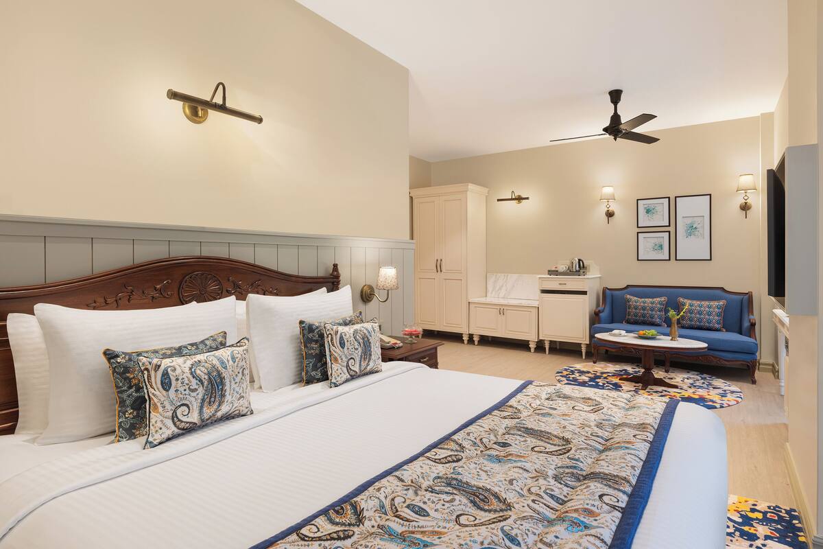 A hotel room with a large bed, a sofa, a desk, and a ceiling fan.