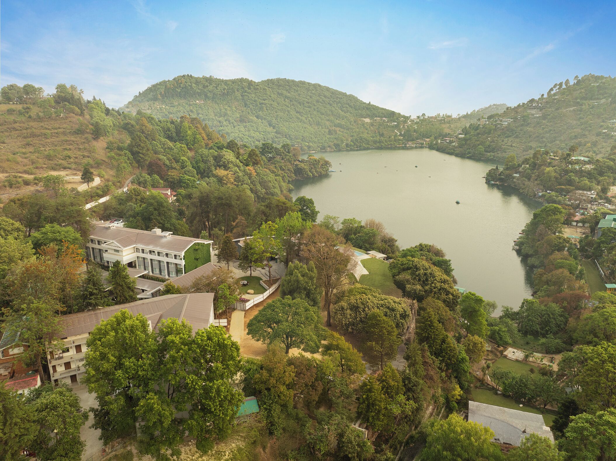 A large building with a green roof, surrounded by trees and a lake.
