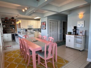A modern kitchen with white cabinets, a central island, and a dining area with pink chairs. - Ocean View 4BR-4BA - Beach Access & Pool + Linens - Pet Friendly (Ocean Isle Beach)