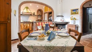 Zona pranzo con camino in mattoni, un tavolo apparecchiato per due e cucina sullo sfondo.