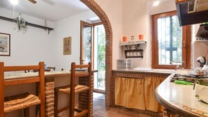 Una cucina con un arco in mattoni, sedie di legno, un tavolo da pranzo e una finestra con vista sul verde.