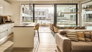 A modern kitchen with a central island, a dining area with a view, and a cozy seating area with a sofa and cushions.
