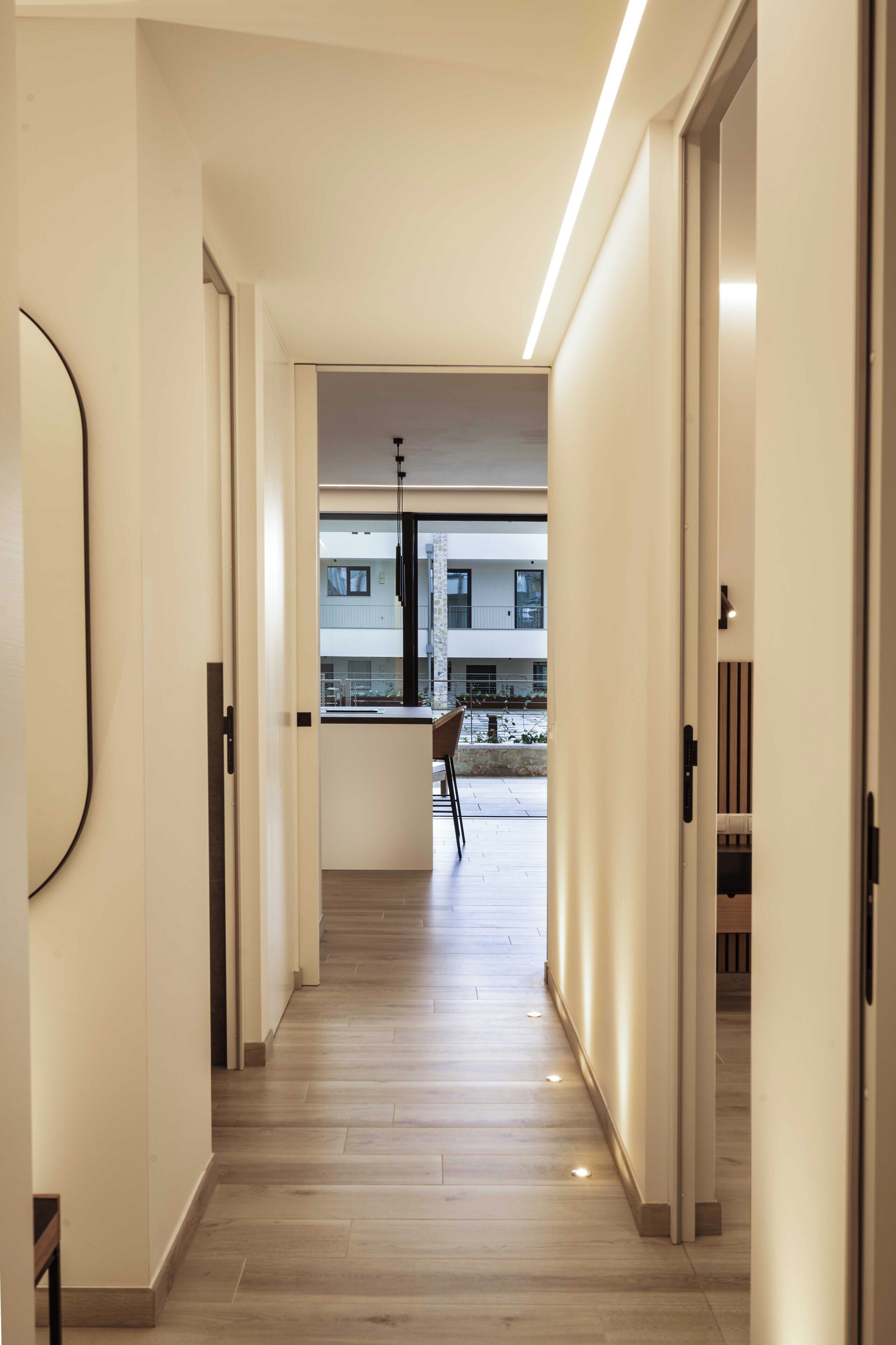 A modern hallway with a wooden floor, leading to a balcony with a view of buildings.
