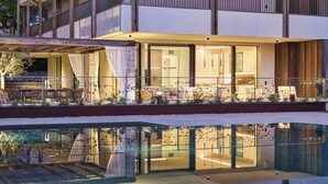 A modern hotel with a pool, outdoor seating, and a well-lit interior.