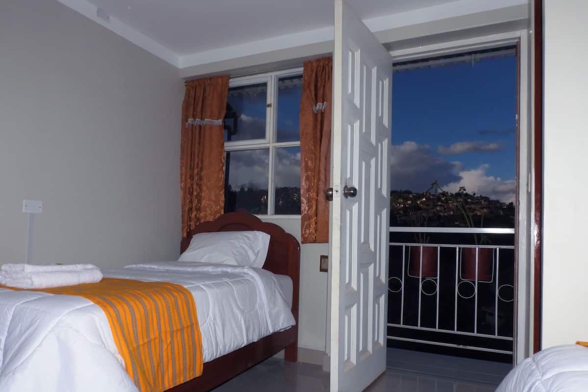 Une chambre à coucher avec un lit, une fenêtre avec des rideaux et un balcon doté d’une balustrade.